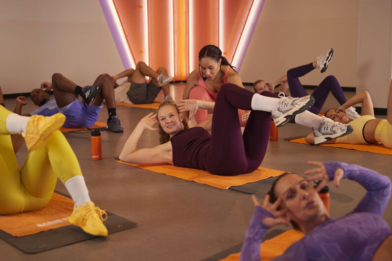 Abs & Core groepsles op matten, met een instructeur die een deelnemer begeleidt tijdens een core-oefening op de vloer.