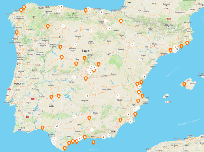 Map of Spain with Basic-Fit club locations marked by orange &ldquo;B&rdquo; icons, spread across major areas including Madrid, Valencia, Barcelona, the Costa del Sol, and the Balearic Islands. Additional clubs are shown in northern and western regions and along the Mediterranean coast.