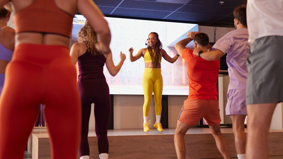 Deelnemers volgen een fat burn cardio-les en bewegen continu samen terwijl ze de instructeur voorin de zaal volgen.