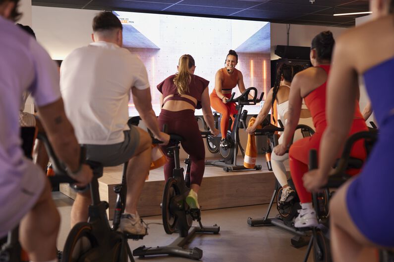 Indoor cycling les, met een instructeur op een spinningfiets die de les leidt terwijl deelnemers meefietsen.