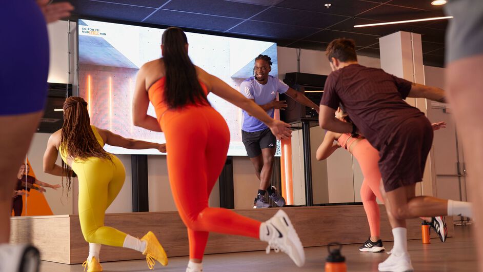 Een groep neemt deel aan een bodycombat-les en voert stootbewegingen uit terwijl ze de instructeur op het podium volgen.