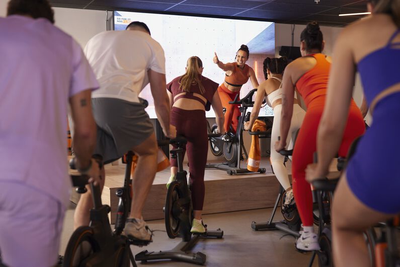 Woman cycling indoors on a stationary bike, leading a virtual workout with enthusiasm in a high-energy studio setting.