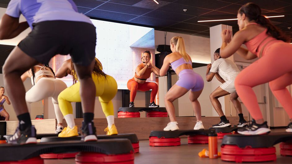 Deelnemers doen een steps-les en voeren squats en stepbewegingen uit op platforms tijdens een groepsles.