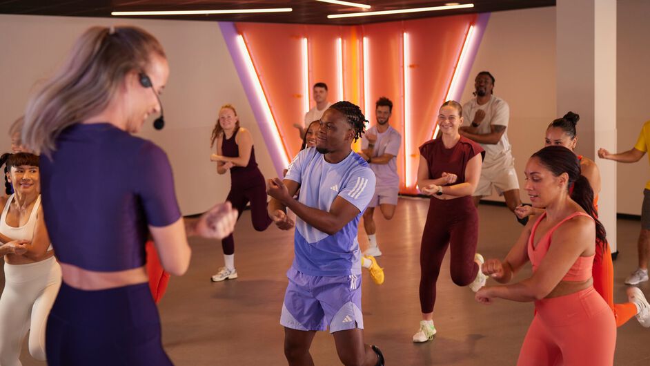 A group takes part in a Zumba class, performing dance steps together while following the instructor in the fitness studio.