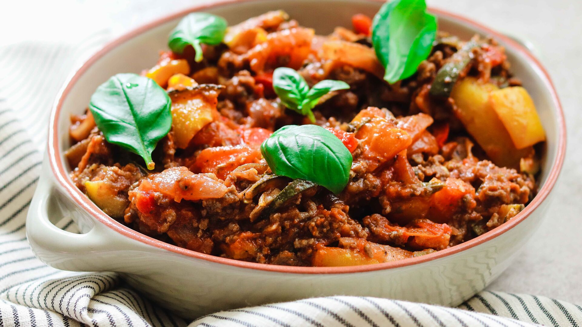 Schüssel mit Fleisch-Gemüse-Ratatouille, garniert mit frischen Basilikumblättern.