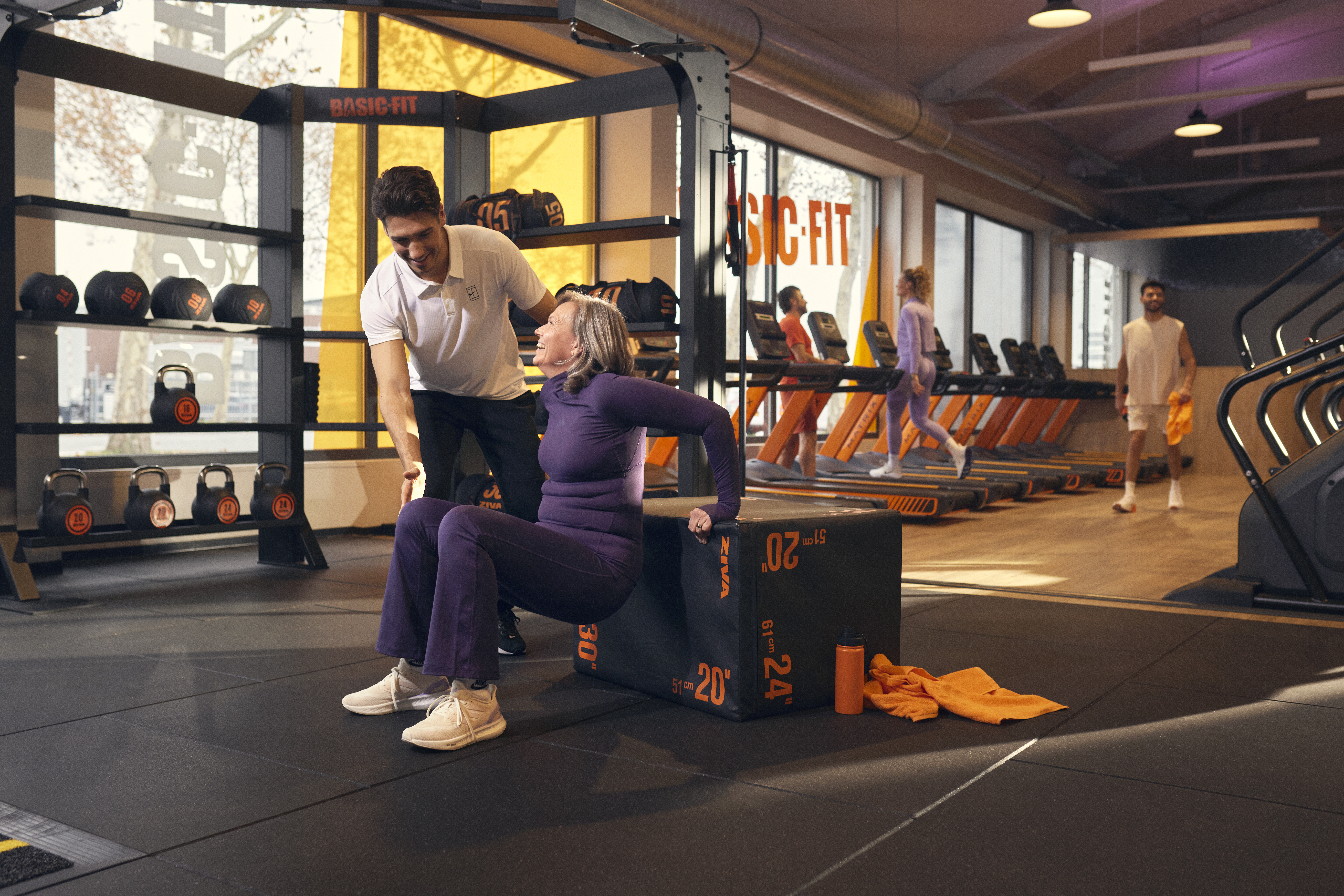 Trainer assisting an older woman with an exercise in the gym.