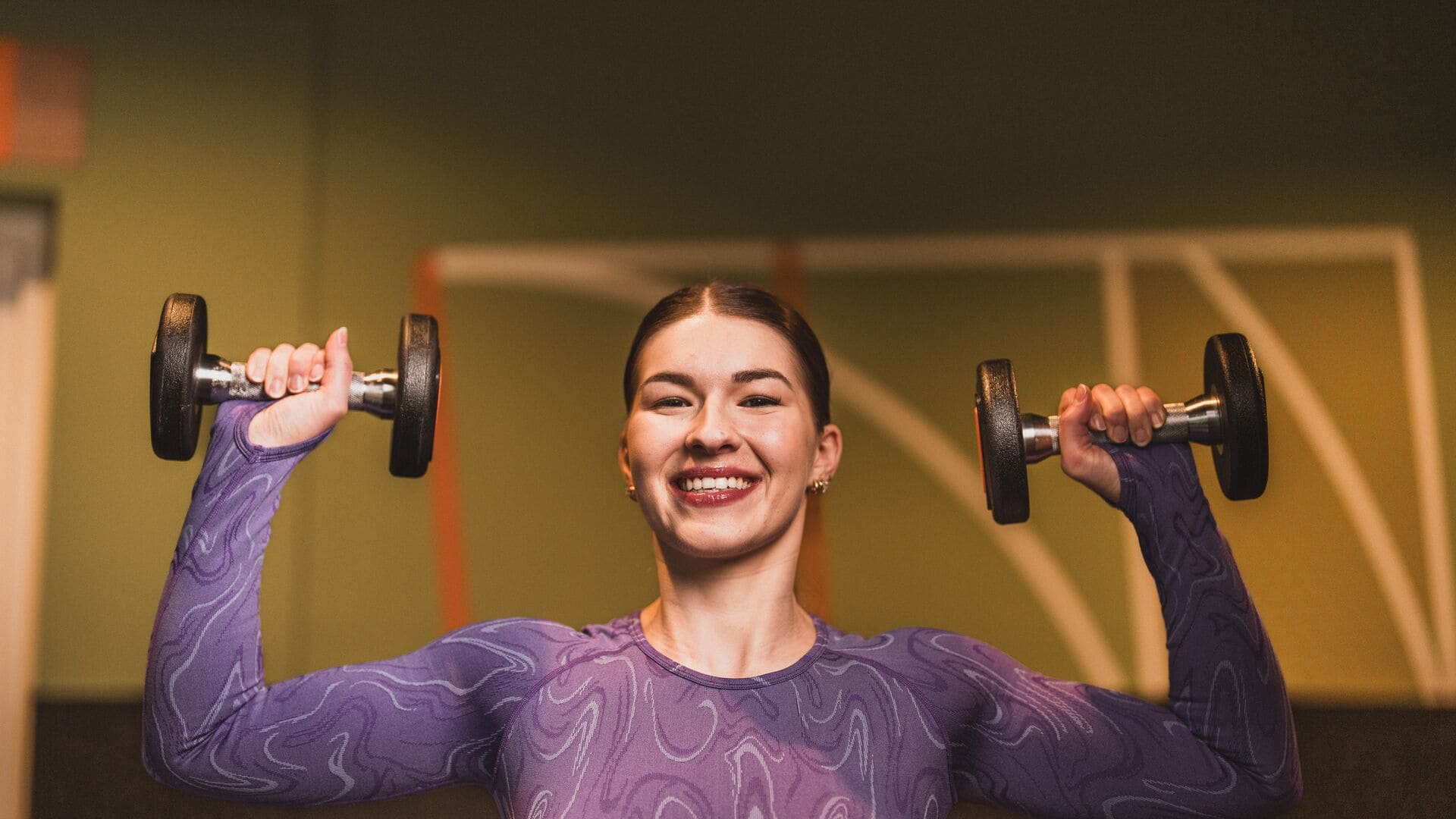 Femme souriante soulevant des haltères pendant son entraînement dans une salle Basic-Fit.