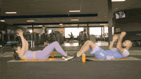 Two people sitting facing each other with feet touching, performing sit-ups and passing a medicine ball back and forth.