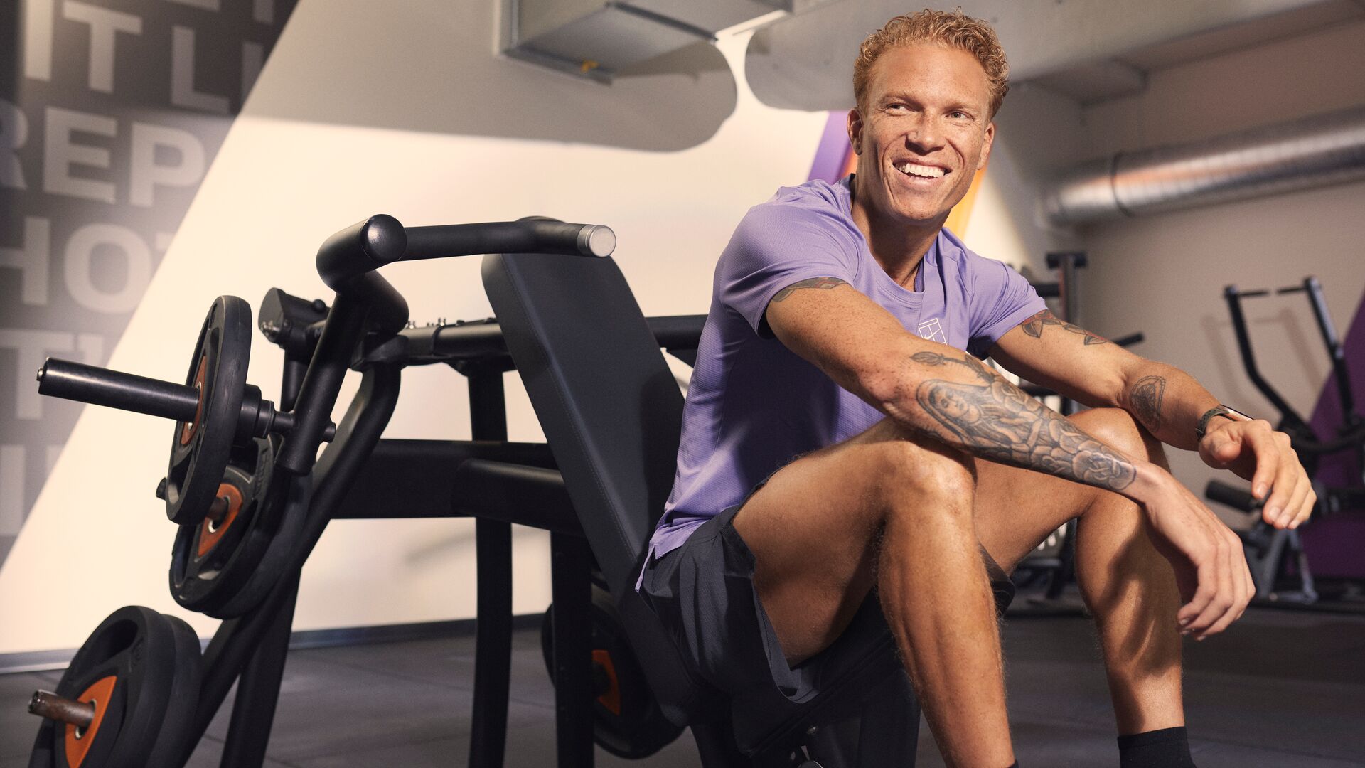 Mann sitzt nach dem Training lächelnd an einem Kraftgerät im Fitnessstudio.