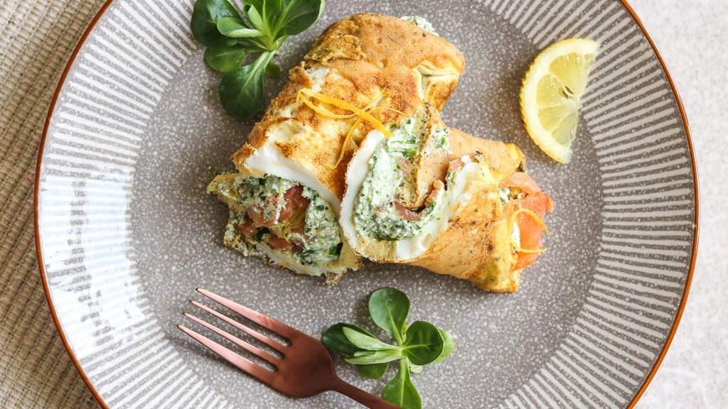 Assiette de wraps à l’omelette garnis de saumon et d’épinards, servie avec du citron et des légumes verts.