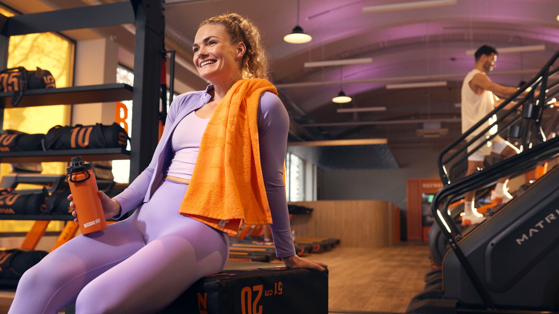 Woman resting after her workout at the gym while a man trains on a stair climber