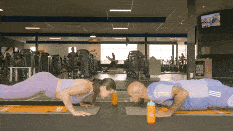 Two people facing each other in a plank position performing synchronized push-ups and clapping.