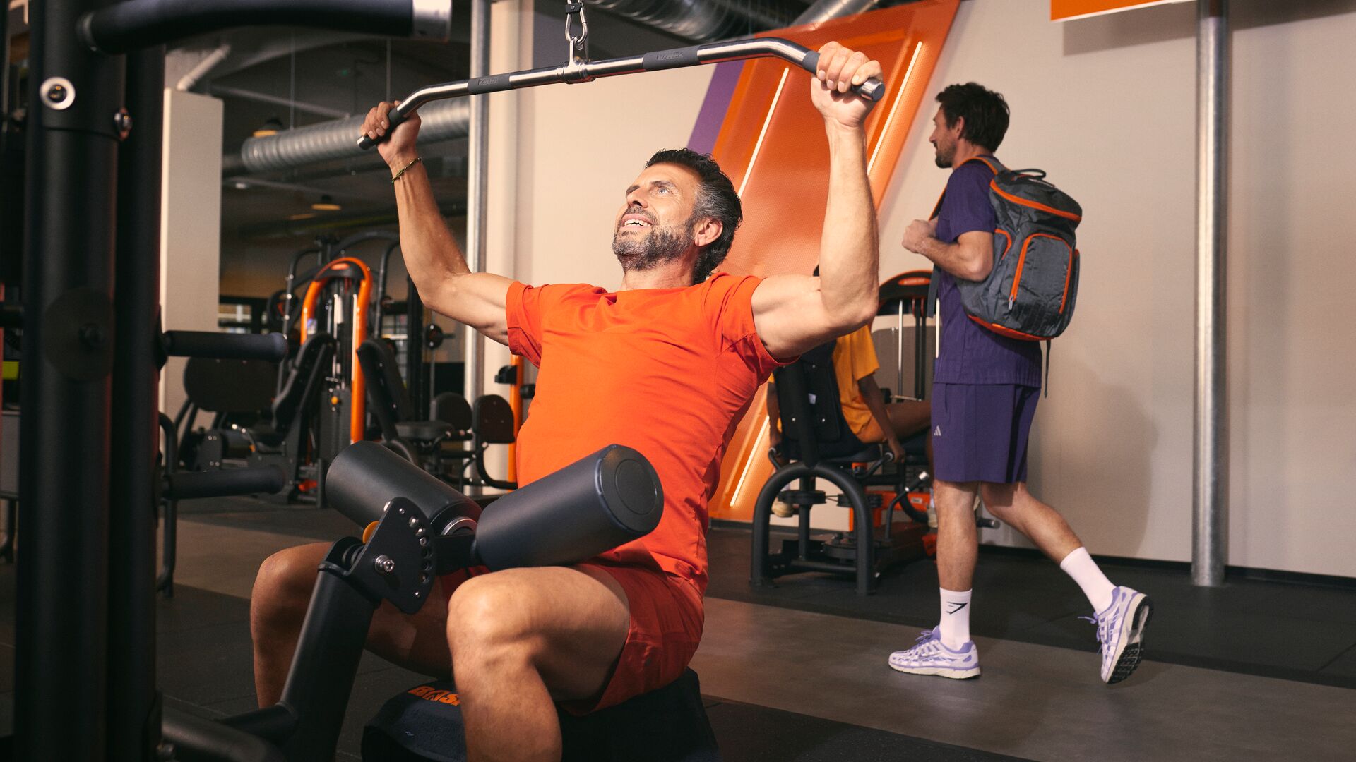 Mann führt ein Latzug-Training an einer Maschine im Fitnessstudio aus.